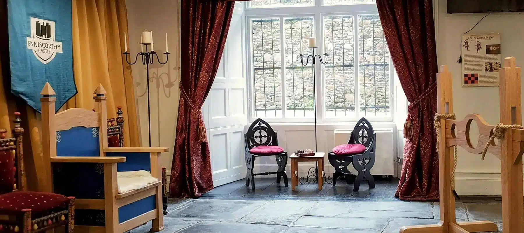 Interior room in Enniscorthy Castle featuring a large window, medieval-style chairs, red curtains and a decorative castle banner.