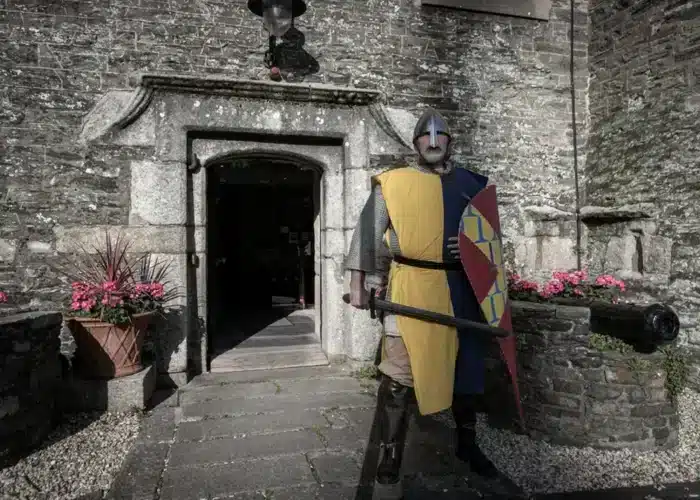 Costumed historical reenactor dressed as a medieval knight standing outside the entrance of Enniscorthy Castle, holding a shield and weapon.