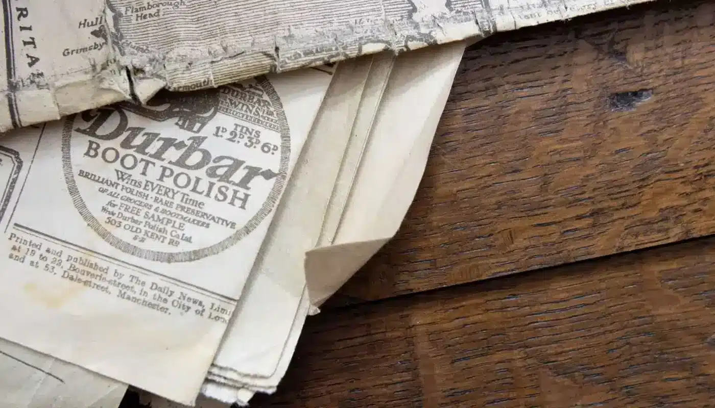 Close-up of old newspaper clippings and vintage advertisements, including one for boot polish, lying on a wooden surface.