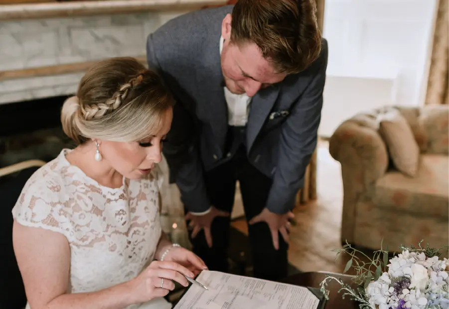 Bride and groom signing their wedding document inside Enniscorthy Castle, with the bride seated and the groom leaning beside her.